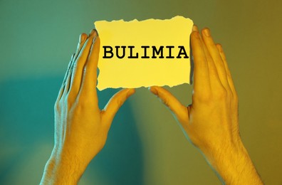 Image of Man holding sheet of paper with word Bulimia on color background, closeup