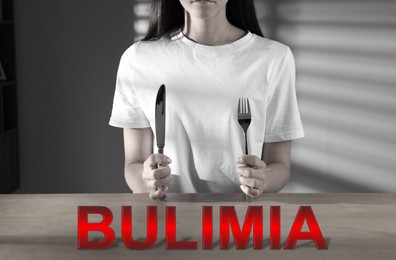 Image of Bulimia nervosa. Woman with cutlery at wooden table indoors, closeup. Black-and-white effect