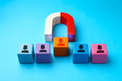 Image of Magnet attracting one of colorful cubes with human figures on light blue background. Recruitment or customer acquisition