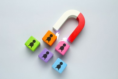 Image of Magnet attracting colorful cubes with human figures on light grey background. Recruitment or customer acquisition