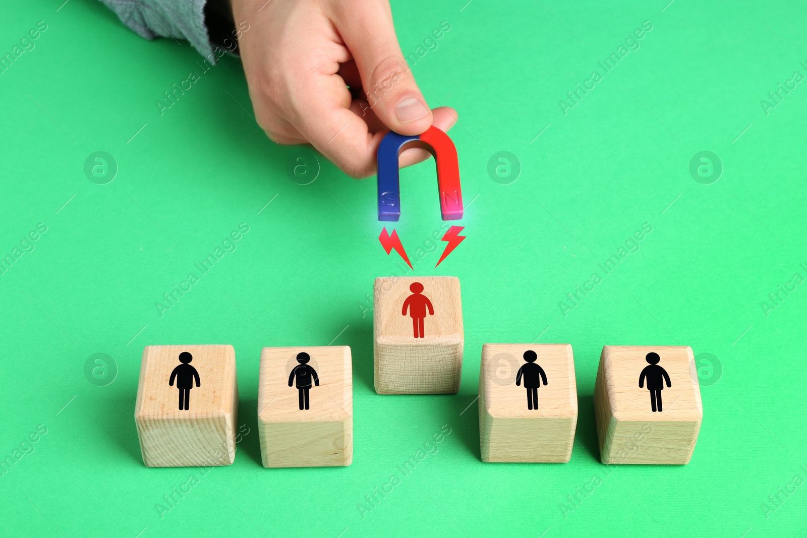 Image of Man with magnet attracting one of wooden cubes on green background, closeup. Recruitment or customer acquisition