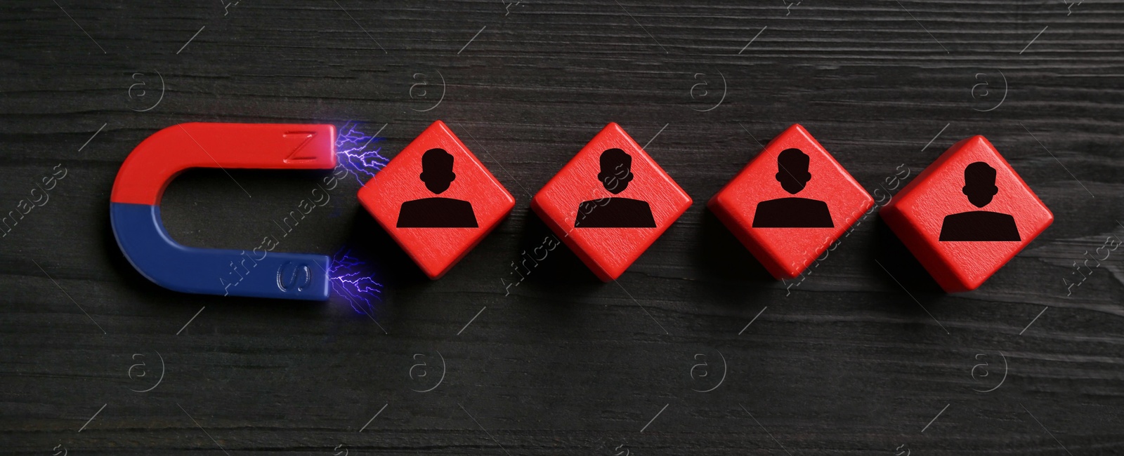 Image of Magnet attracting red cubes with human figures on black wooden background, top view. Recruitment or customer acquisition