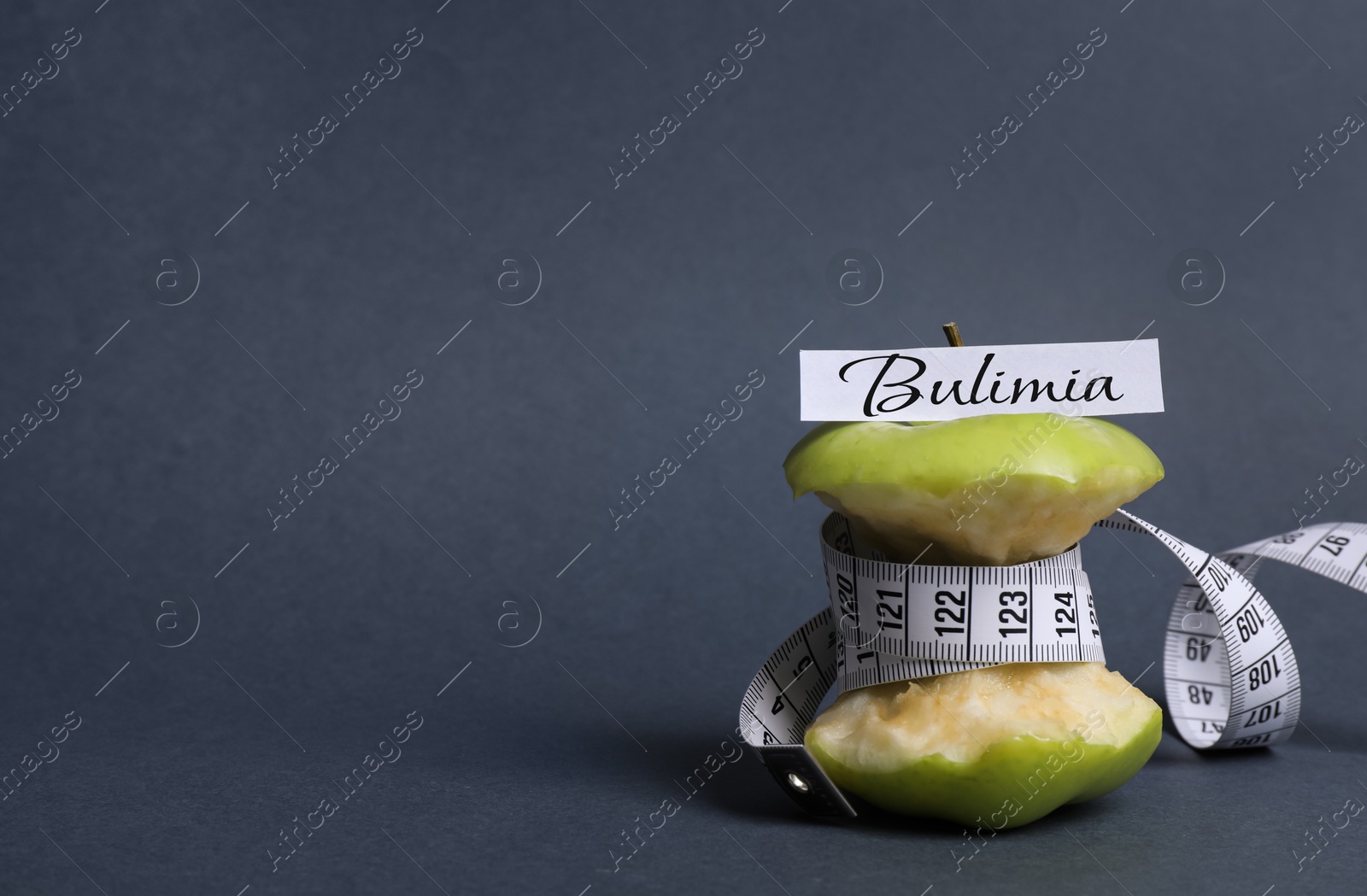 Image of Apple core with measuring tape and word Bulimia on dark grey background, space for text