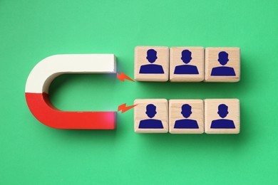 Image of Magnet attracting wooden cubes with human figures on green background, top view. Recruitment or customer acquisition