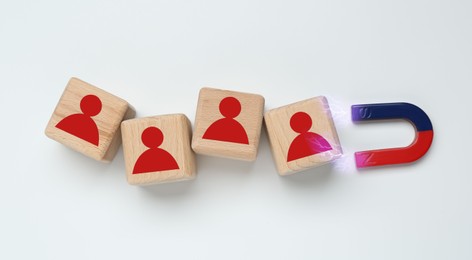 Image of Magnet attracting wooden cubes with human figures on white background, top view. Recruitment or customer acquisition