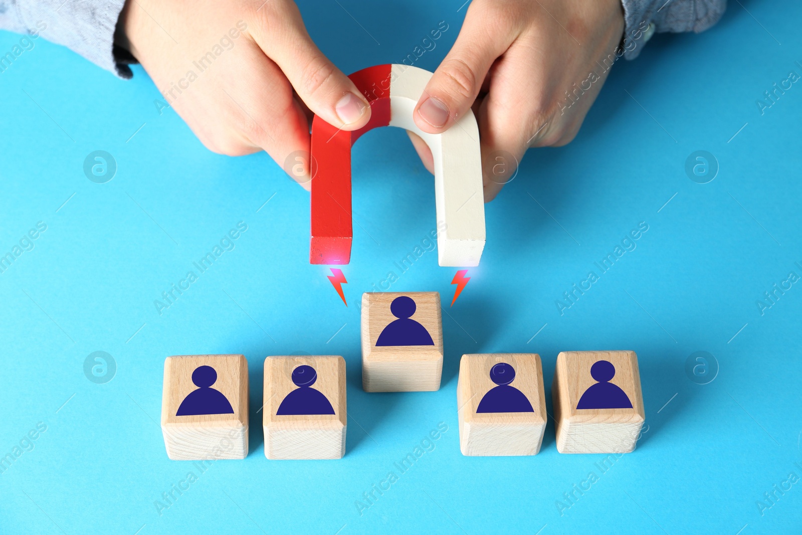 Image of Man attracting one of wooden cubes with magnet on light blue background, closeup. Recruitment or customer acquisition