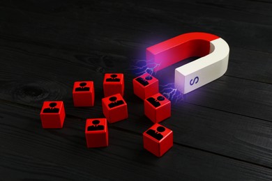 Image of Magnet attracting red cubes with human figures on back wooden background. Recruitment or customer acquisition