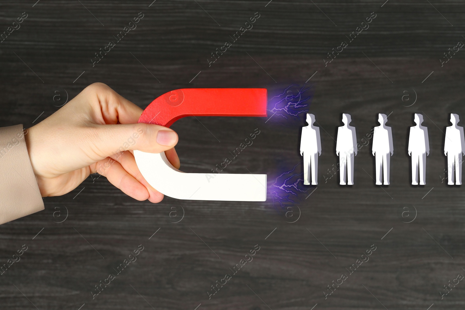 Image of Woman attracting white human figures with magnet on wooden background, closeup. Recruitment or customer acquisition