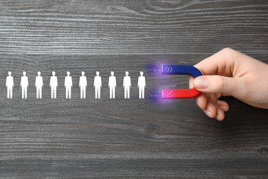 Image of Woman attracting white human figures with magnet on wooden background, closeup. Recruitment or customer acquisition