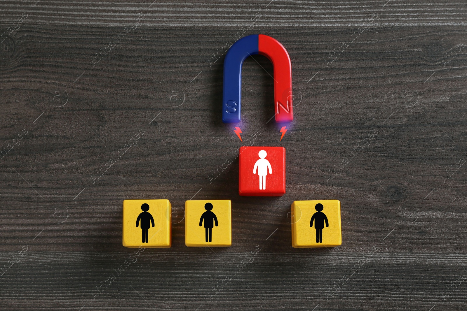 Image of Magnet attracting one of cubes with human figures on wooden background, top view. Recruitment or customer acquisition