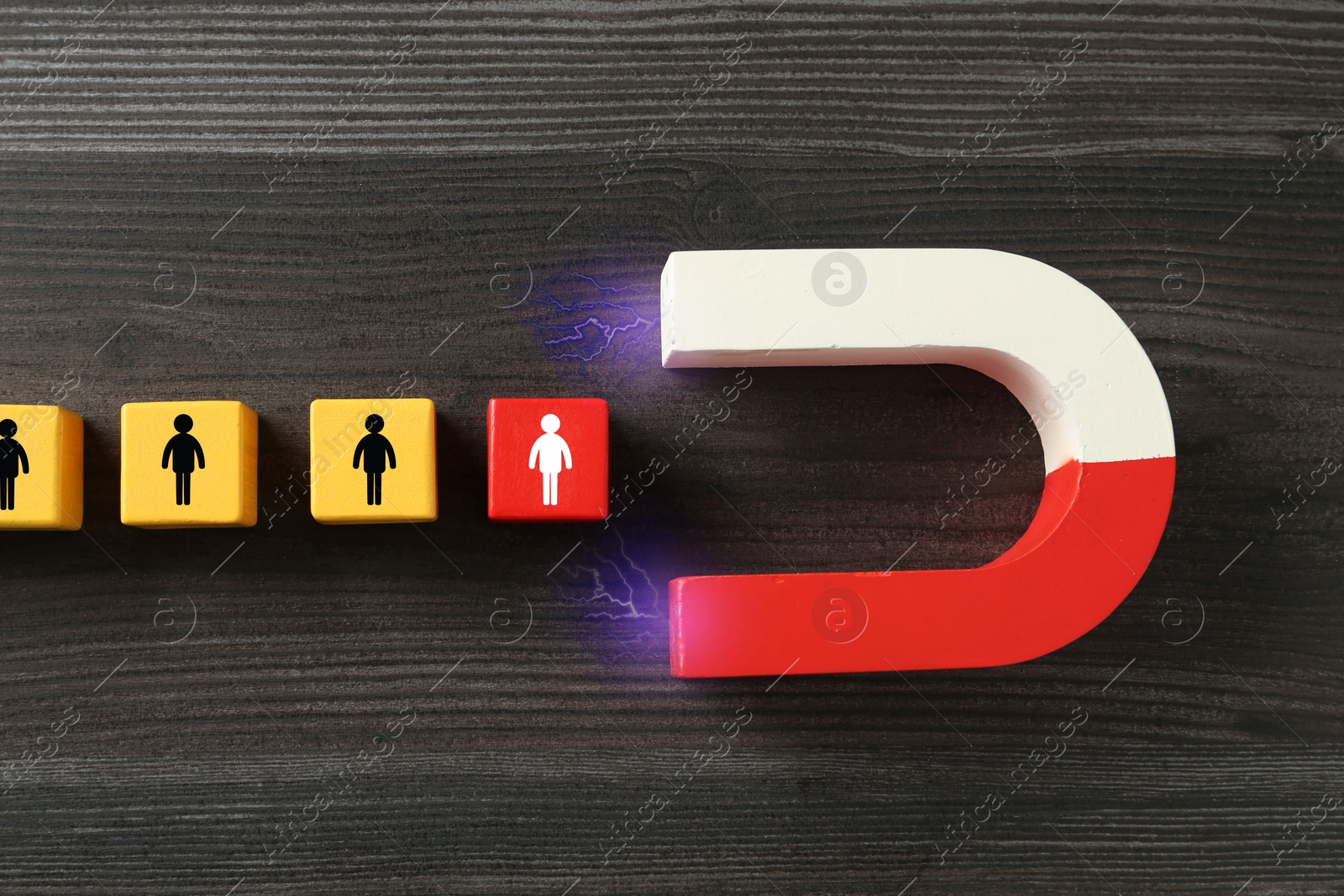 Image of Magnet attracting cubes with human figures on wooden background, top view. Recruitment or customer acquisition