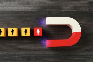 Image of Magnet attracting cubes with human figures on wooden background, top view. Recruitment or customer acquisition