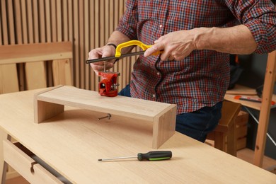 Photo of Relaxing hobby. Senior man with hacksaw and vise assembling wooden shelf in workshop, closeup