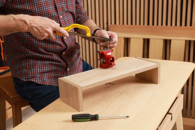 Photo of Relaxing hobby. Senior man with hacksaw and vise assembling wooden shelf in workshop, closeup