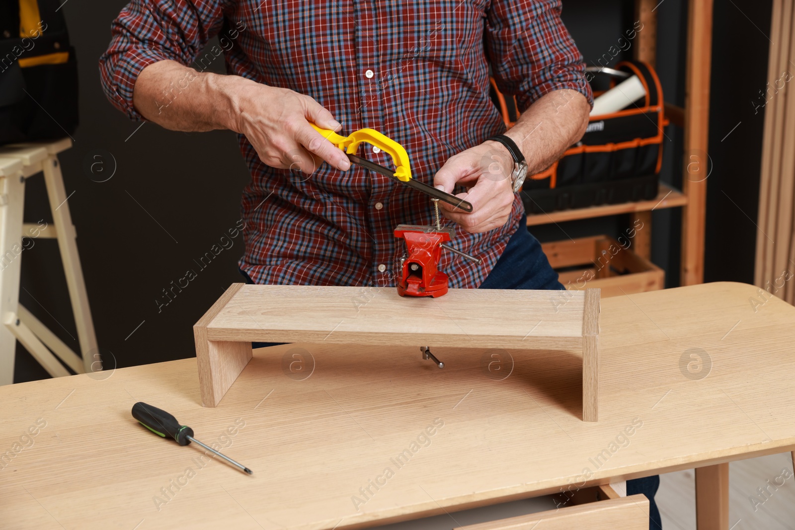 Photo of Relaxing hobby. Senior man with hacksaw and vise assembling wooden shelf in workshop, closeup