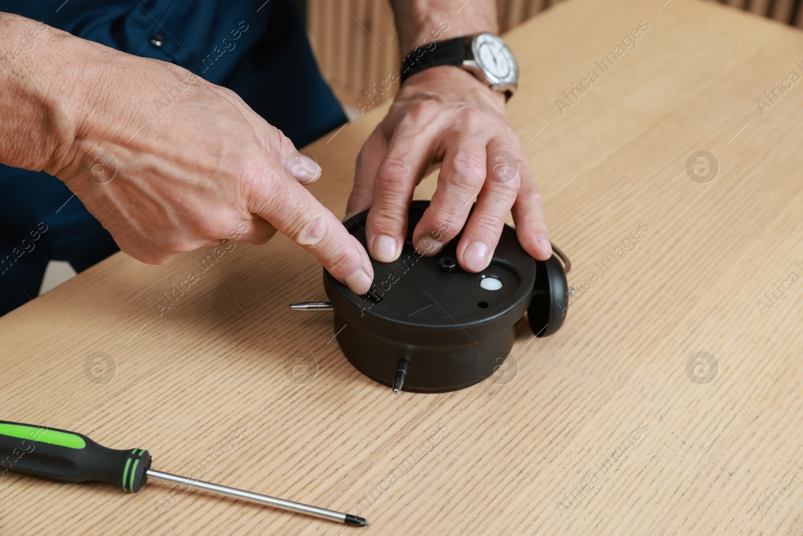 Photo of Relaxing hobby. Senior man repairing alarm clock at wooden table in workshop, closeup