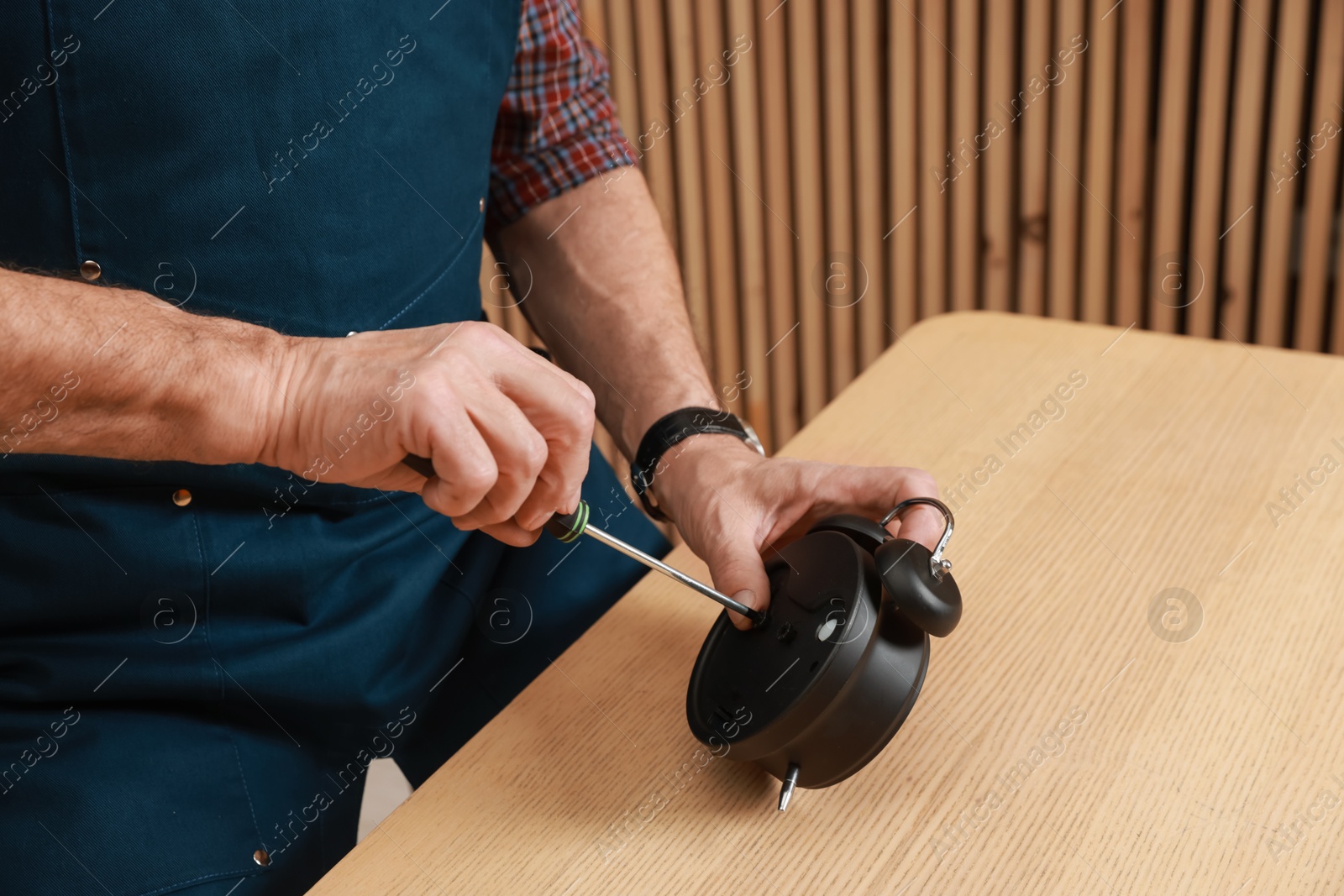 Photo of Relaxing hobby. Senior man repairing alarm clock at wooden table in workshop, closeup