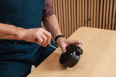 Photo of Relaxing hobby. Senior man repairing alarm clock at wooden table in workshop, closeup