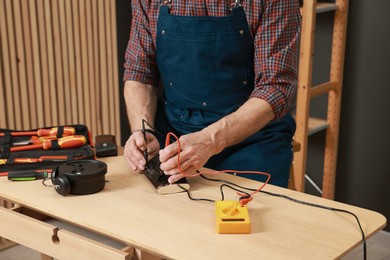 Photo of Relaxing hobby. Senior man testing alarm clock with multimeter in workshop, closeup