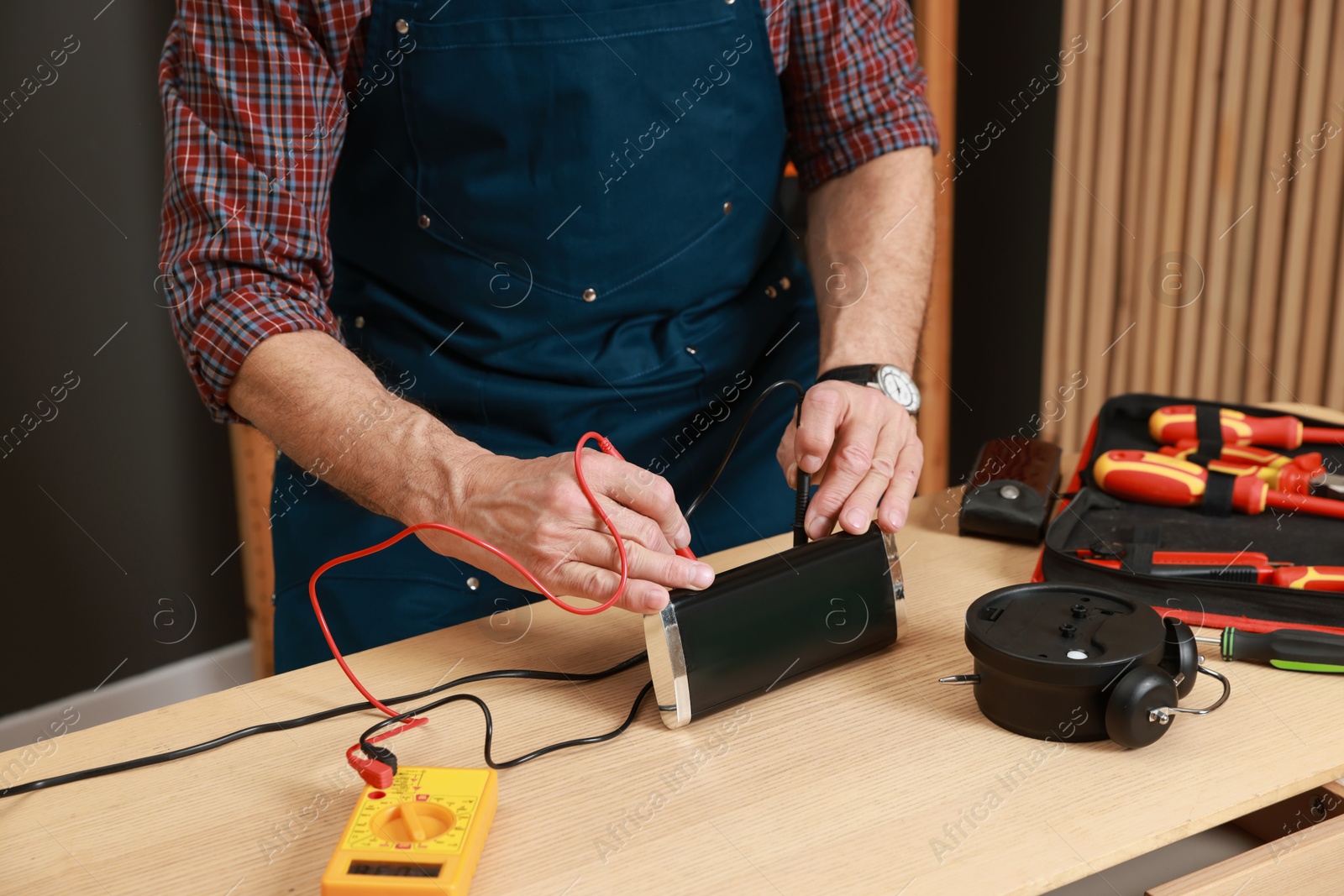 Photo of Relaxing hobby. Senior man testing alarm clock with multimeter in workshop, closeup