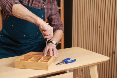 Photo of Relaxing hobby. Senior man repairing wooden jewelry box with screwdriver in workshop, closeup