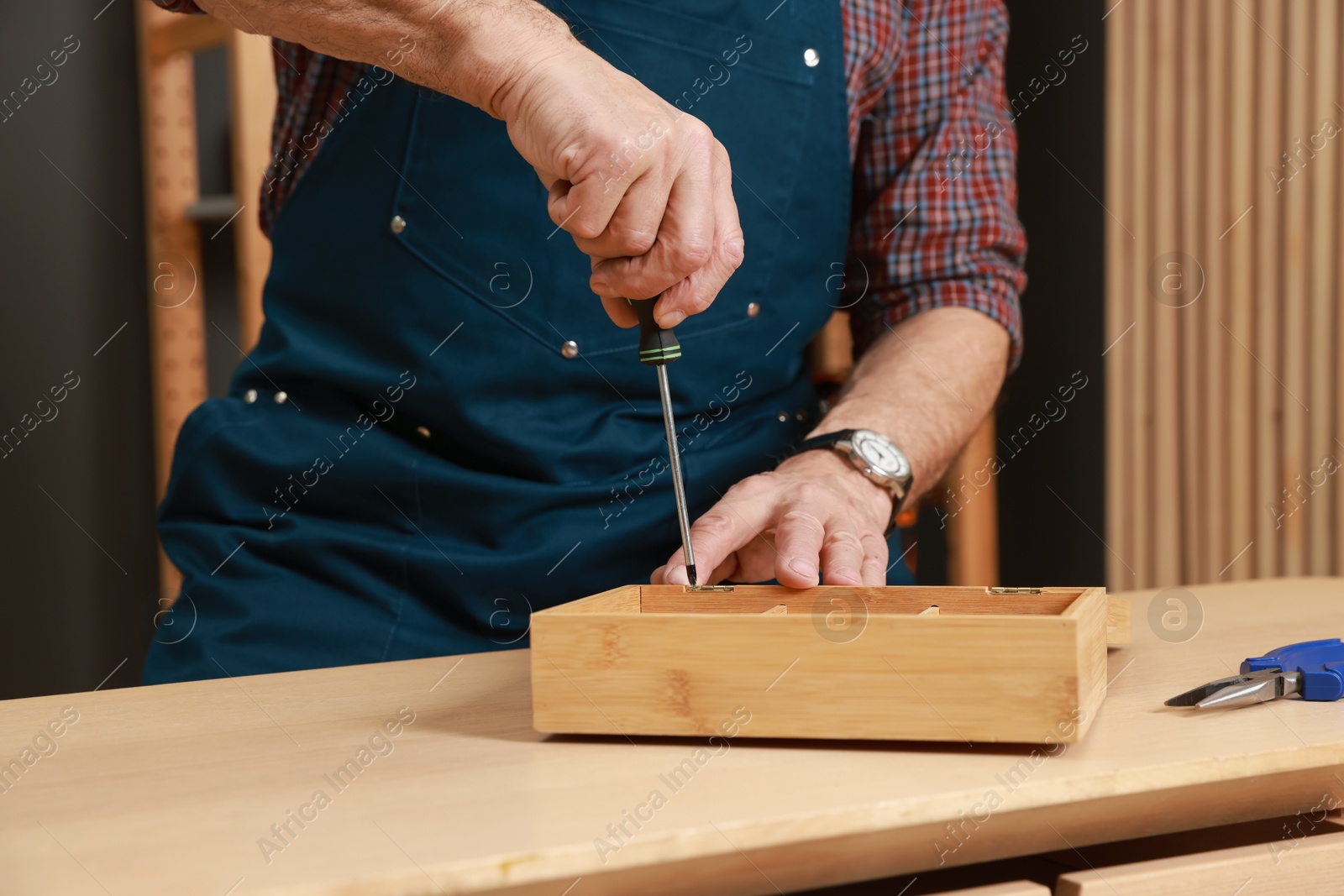 Photo of Relaxing hobby. Senior man repairing wooden jewelry box with screwdriver in workshop, closeup