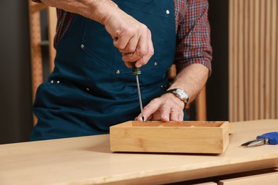 Photo of Relaxing hobby. Senior man repairing wooden jewelry box with screwdriver in workshop, closeup