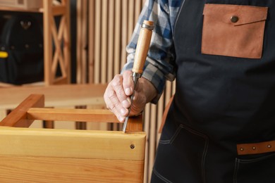 Photo of Relaxing hobby. Senior man repairing wooden stool with chisel in workshop, closeup