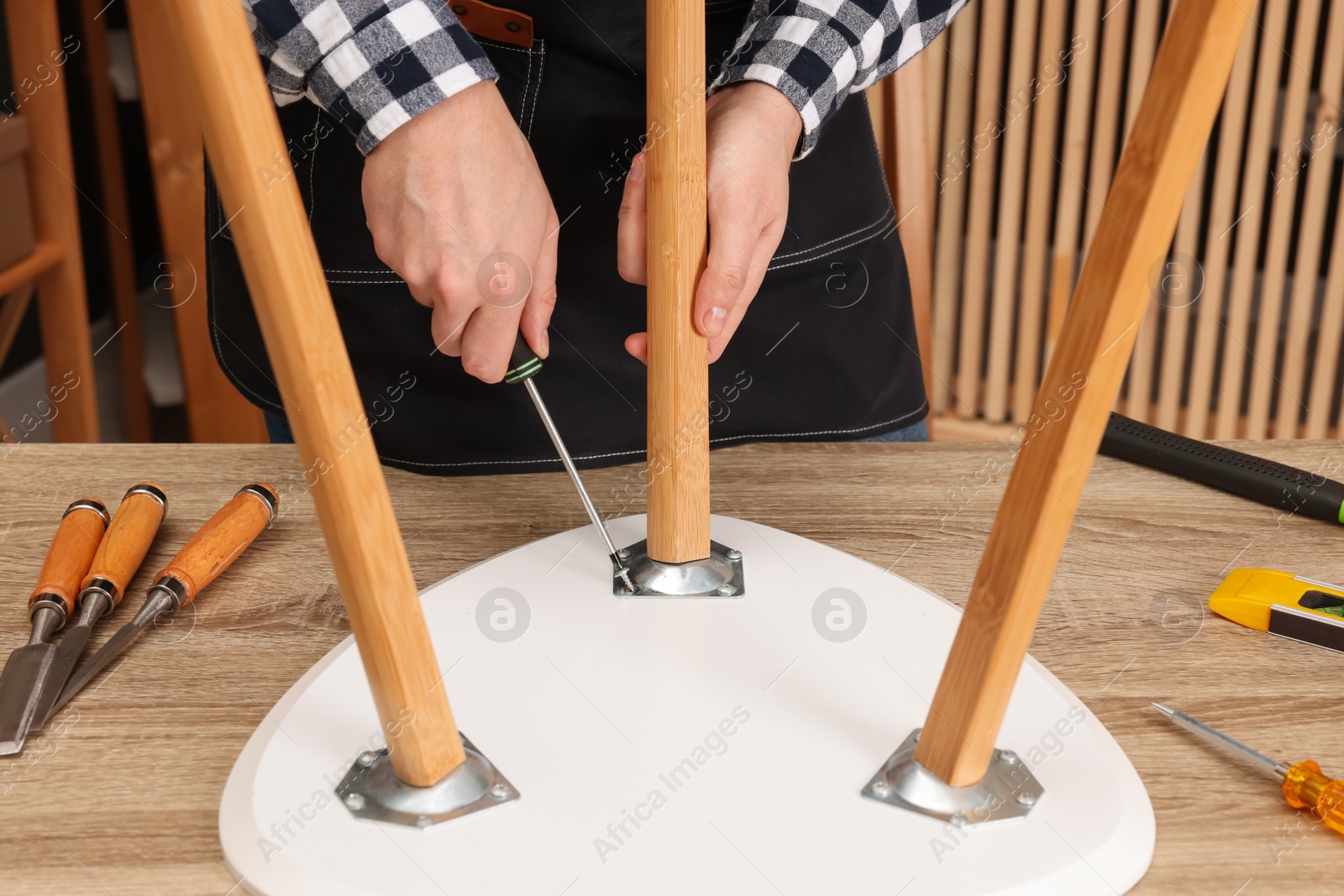 Photo of Relaxing hobby. Man assembling stool with screwdriver at wooden table in workshop, closeup