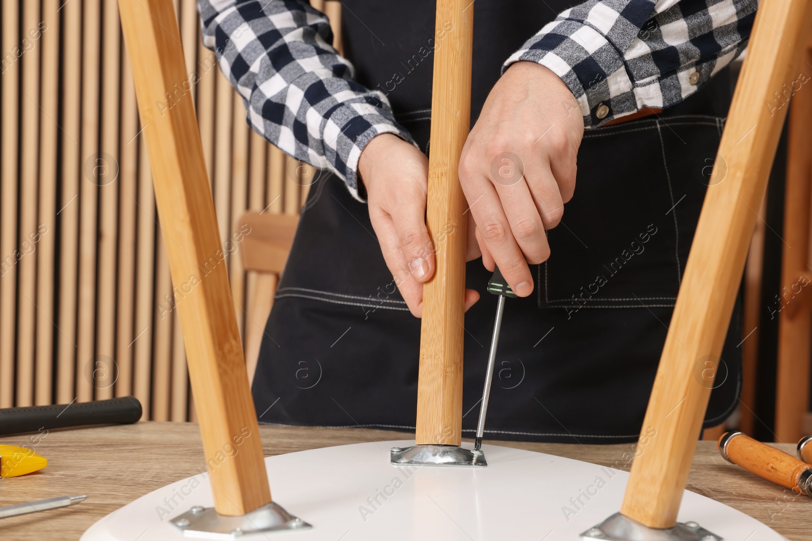 Photo of Relaxing hobby. Man assembling stool with screwdriver at wooden table in workshop, closeup