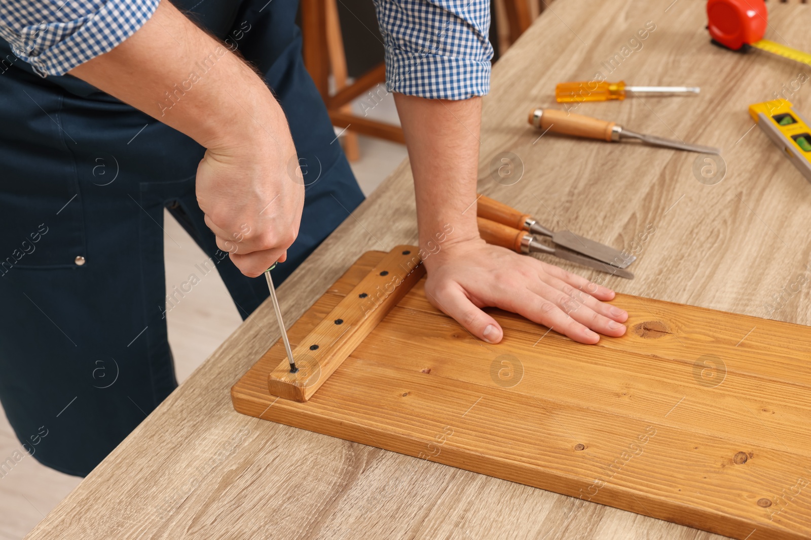 Photo of Relaxing hobby. Man working with wooden plank and screwdriver at table indoors, closeup