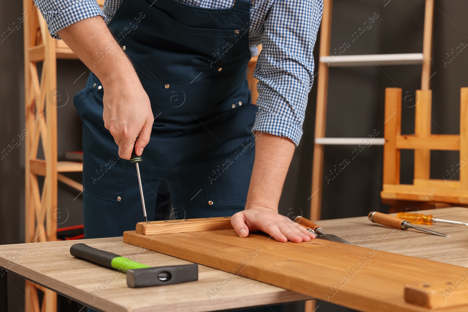 Photo of Relaxing hobby. Man working with wooden plank and screwdriver at table indoors, closeup