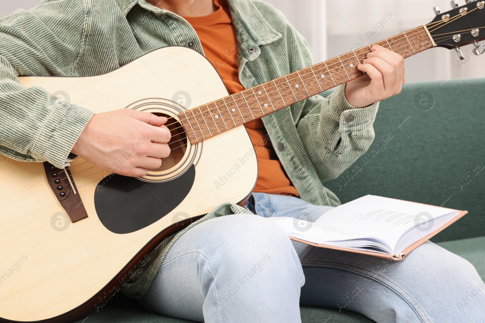 Photo of Relaxing hobby. Man with guitar and book on sofa at home, closeup