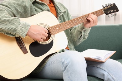 Photo of Relaxing hobby. Man with guitar and book on sofa at home, closeup