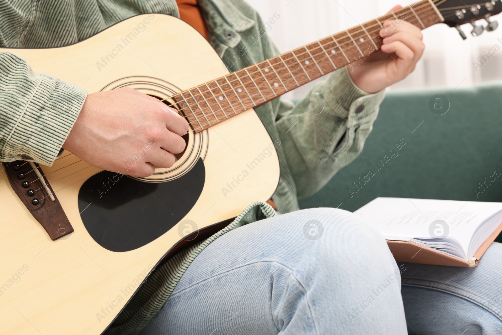 Photo of Relaxing hobby. Man with guitar and book on sofa at home, closeup