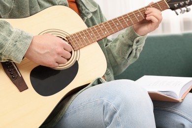 Photo of Relaxing hobby. Man with guitar and book on sofa at home, closeup