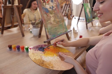 Smiling woman with palette and brush learning to draw at table in class