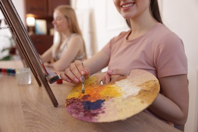 Photo of Smiling woman with palette and brush learning to draw at table in class, closeup