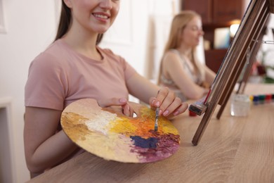 Smiling woman with palette and brush learning to draw at table in class, closeup