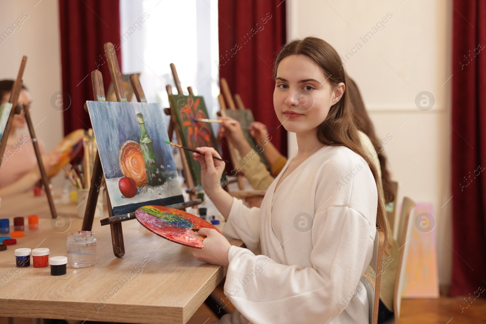 Photo of Young woman with palette and brush learning to draw at table in class