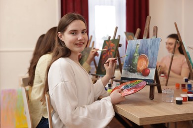 Photo of Smiling woman with palette and brush learning to draw at table in class