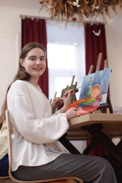 Photo of Smiling woman with palette and brush learning to draw at table in class