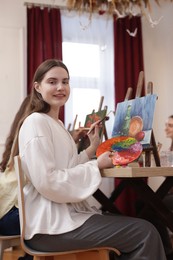 Photo of Smiling woman with palette and brush learning to draw at table in class