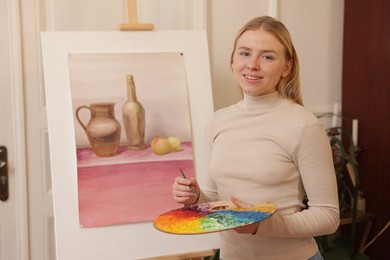 Smiling woman with palette and brush learning to draw in class