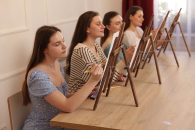 Photo of Group of women with easels learning to draw at wooden table in class