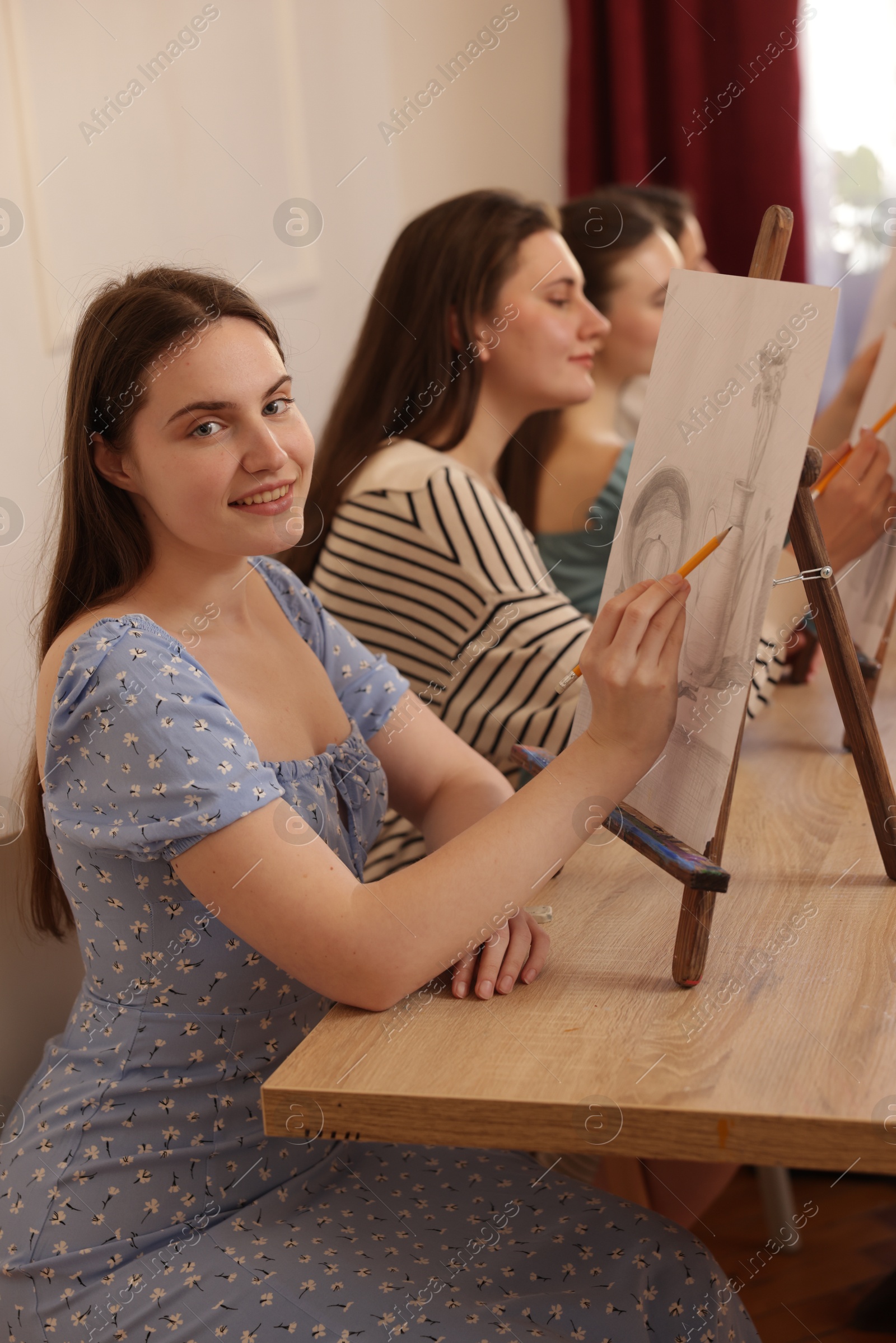 Photo of Group of women with easels learning to draw at wooden table in class