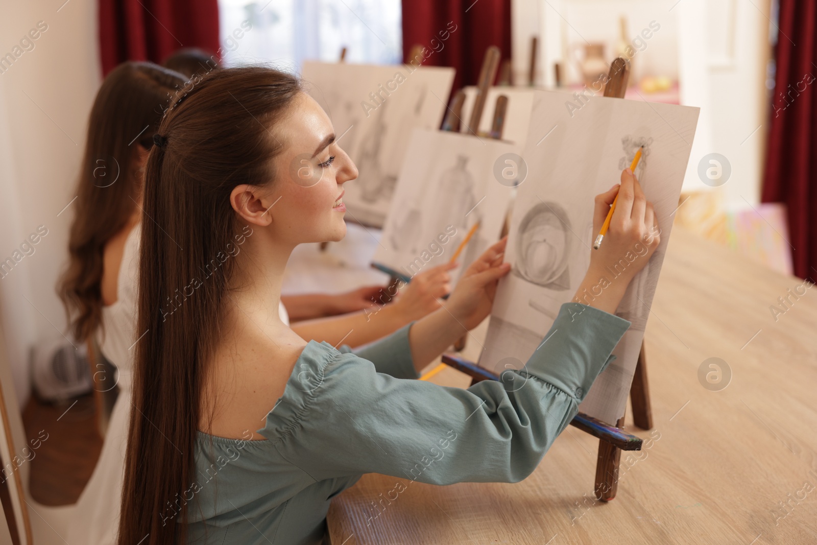 Photo of Group of women with easels learning to draw pictures at wooden table indoors