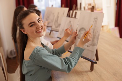 Group of women with easels learning to draw pictures at wooden table indoors