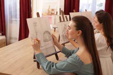 Photo of Group of women with easels learning to draw pictures at wooden table indoors