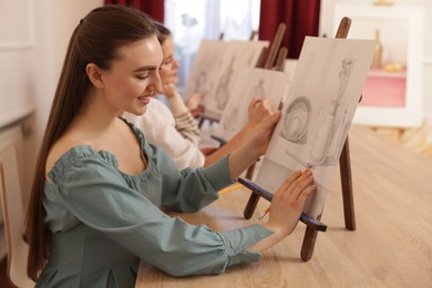 Photo of Group of women with easels learning to draw pictures at wooden table indoors